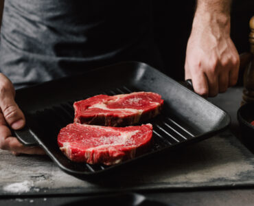 Man cooking beef steaks Male hands holding a grill pan with beef steaks on kitchen