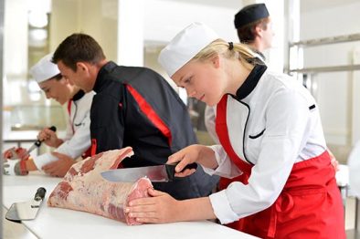 Girl cutting meat during butcher training course